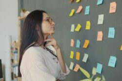 Thoughtful woman planning ideas on a chalkboard wall with colorful sticky notes in an office setting.
